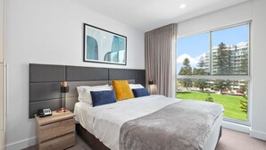 Une chambre moderne avec un grand lit, une table de chevet avec une lampe et une vue sur le paysage urbain, visible à travers une grande fenêtre.