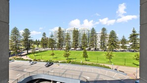 On voit un parking avec plusieurs voitures, un champ d’herbe et, au fond, une rangée d’immeubles d’appartements modernes.