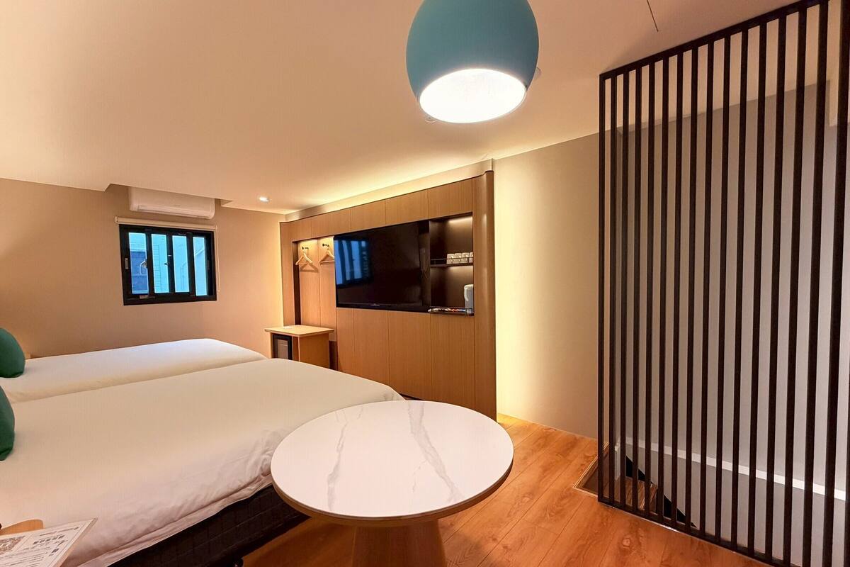 Una habitación de hotel moderna con una cama, una mesita redonda pequeña, un televisor y una ventana.
