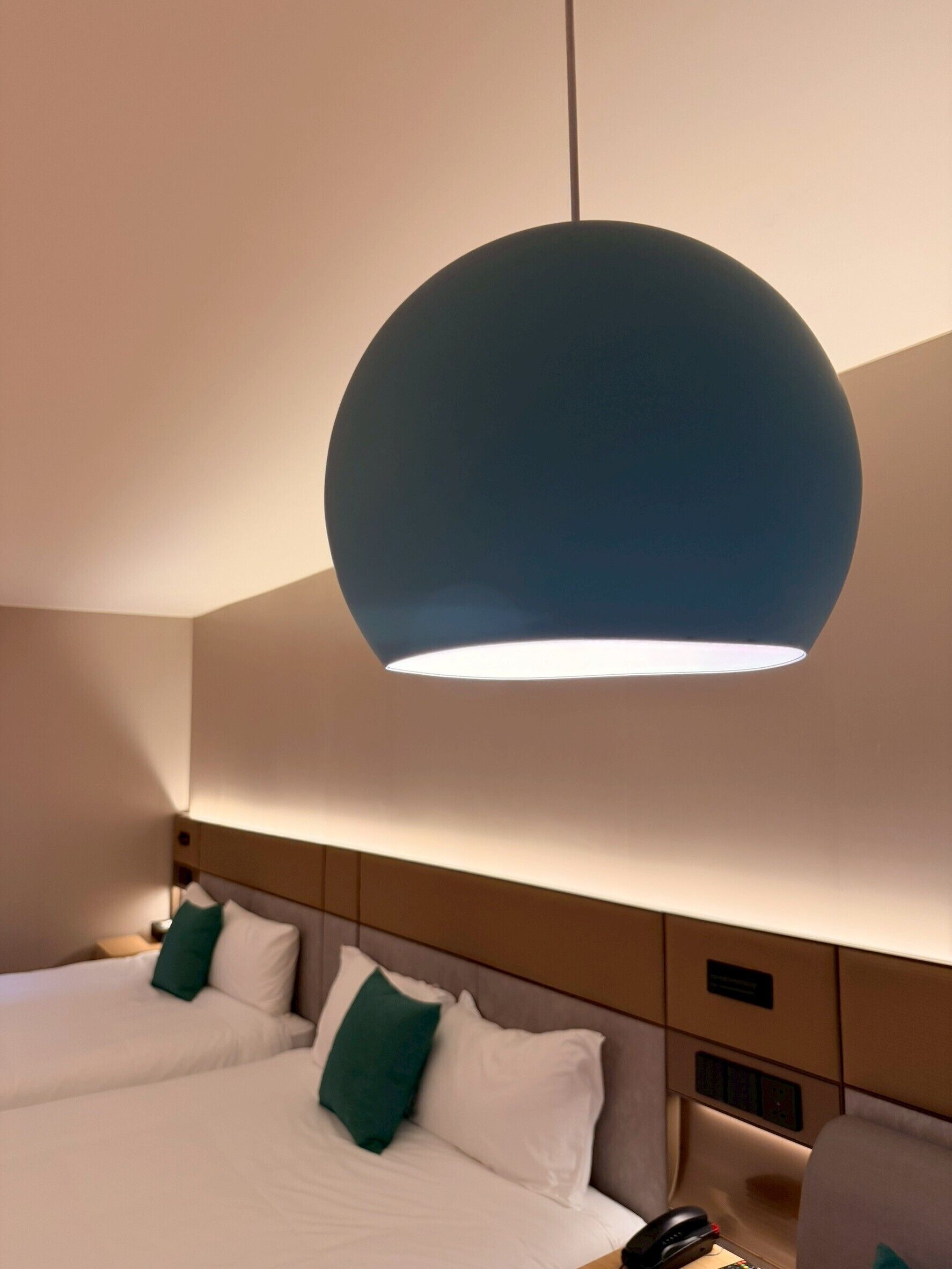 Une chambre d’hôtel avec deux lits, un grand luminaire suspendu bleu et une table de chevet avec un téléphone.