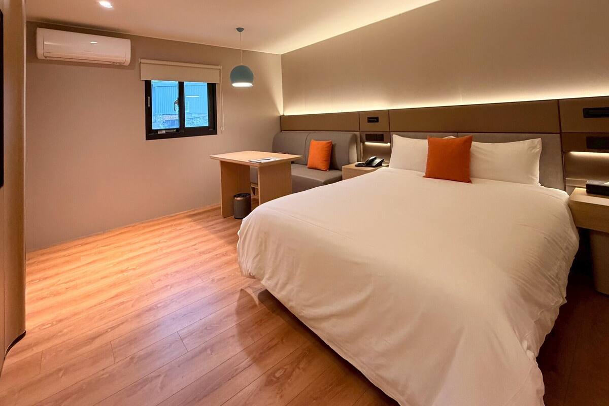 Habitación de hotel con una cama grande, un escritorio, una silla, un cesto de basura y una ventana.
