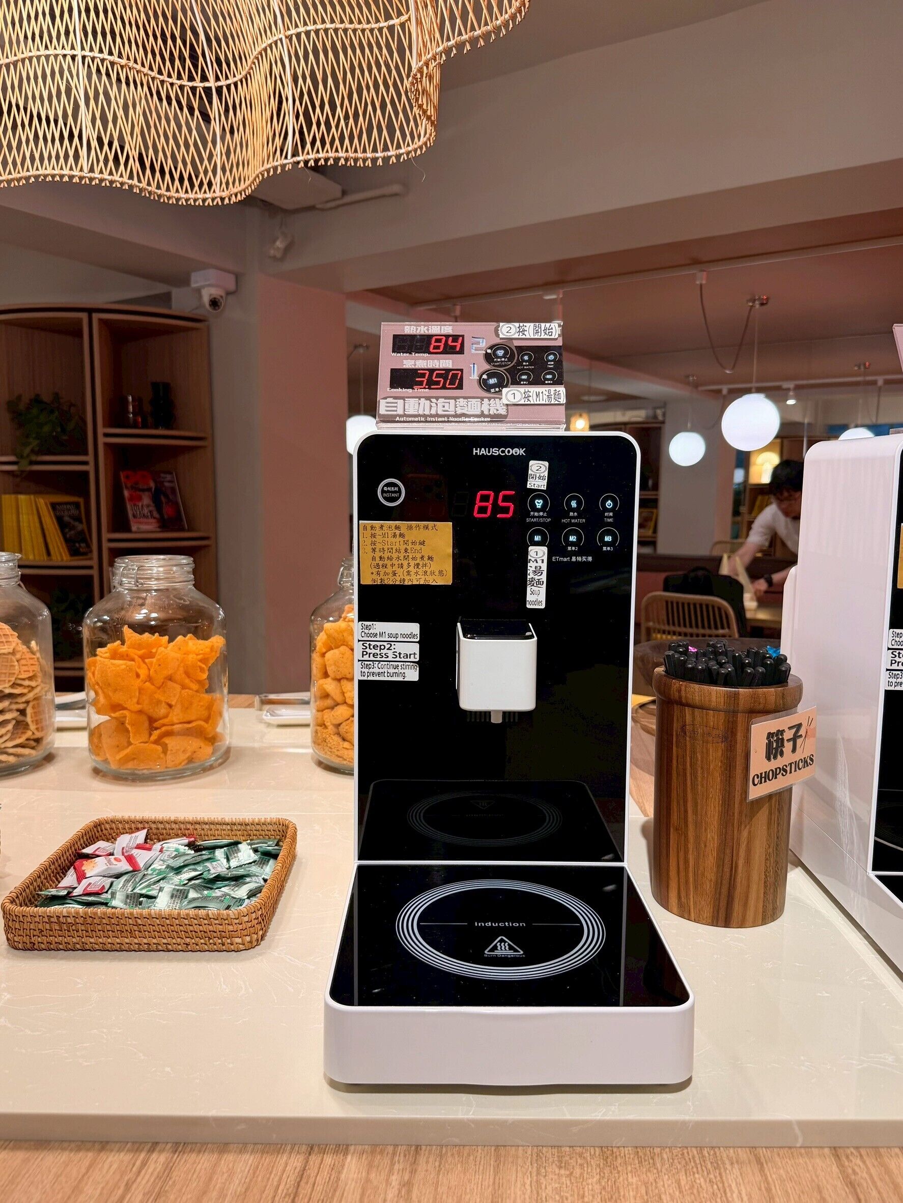 Une cuisine équipée d’une plaque de cuisson à induction moderne, d’un écran numérique et de divers produits alimentaires, comme des chips et des nouilles.