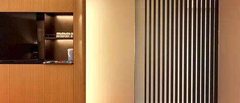 A modern room with a wooden wardrobe, a flat-screen TV, and a sliding door with vertical blinds.