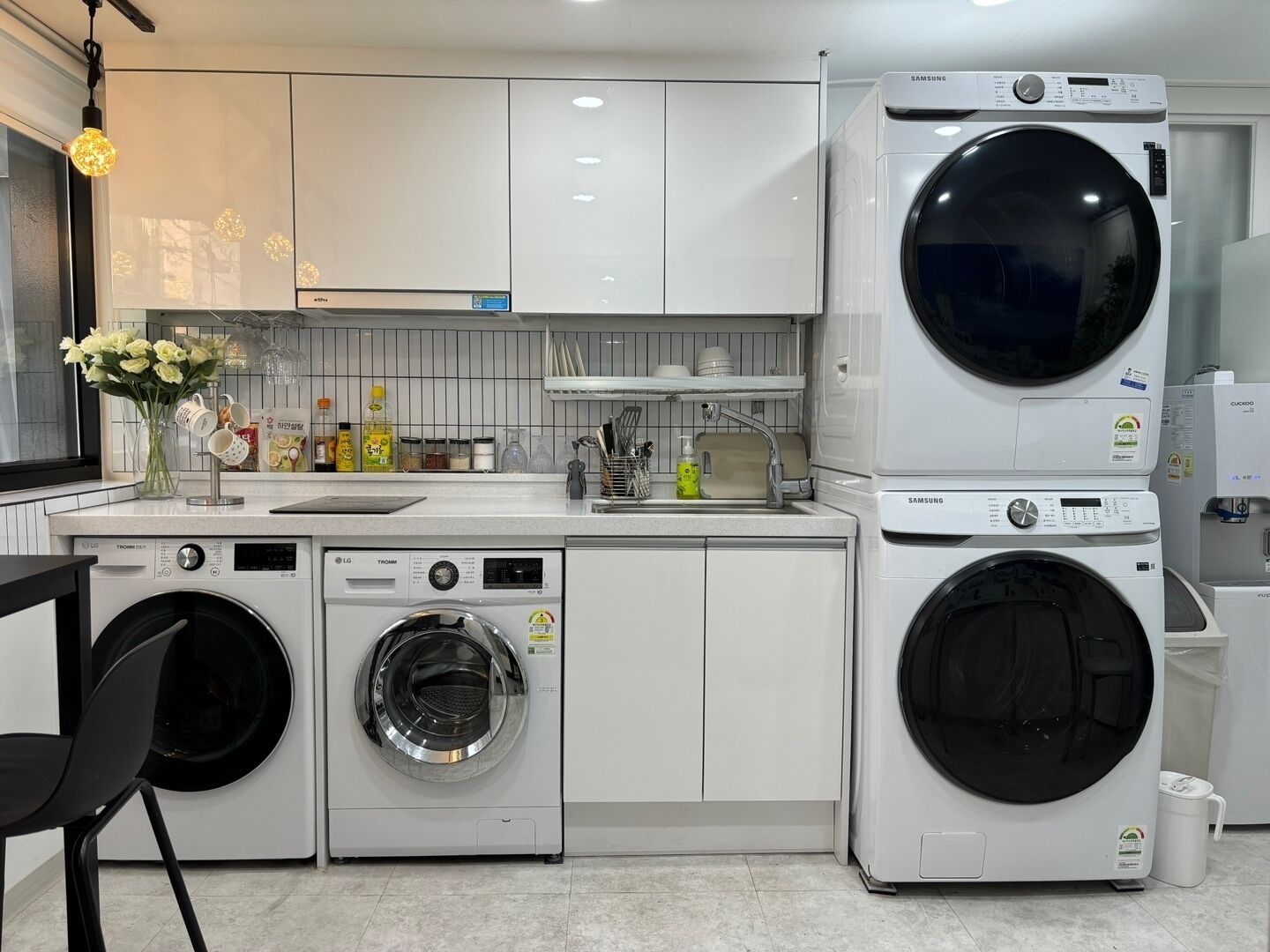 A modern laundry room with two stacked washing machines, a sink, and a countertop with various items.