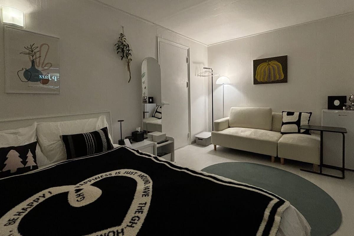 A modern bedroom with a bed, bedside table, lamp, and a sofa.