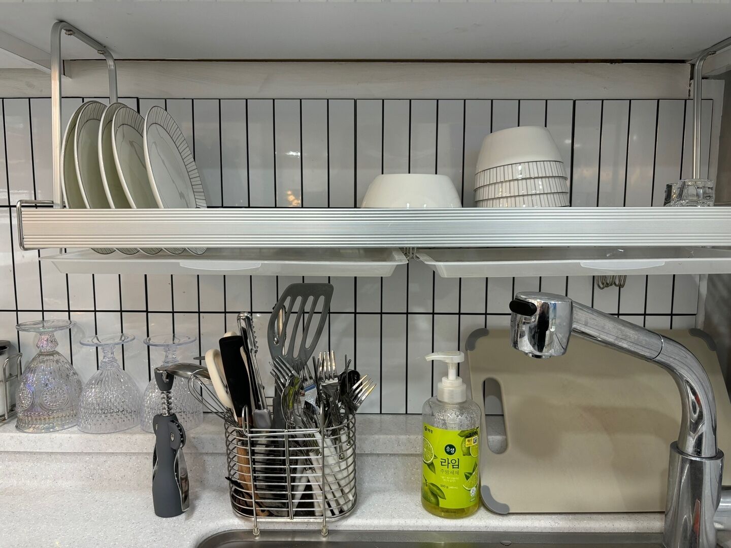 A kitchen with a stainless steel sink, a dish rack above the sink, and a utensil holder with various kitchen tools.