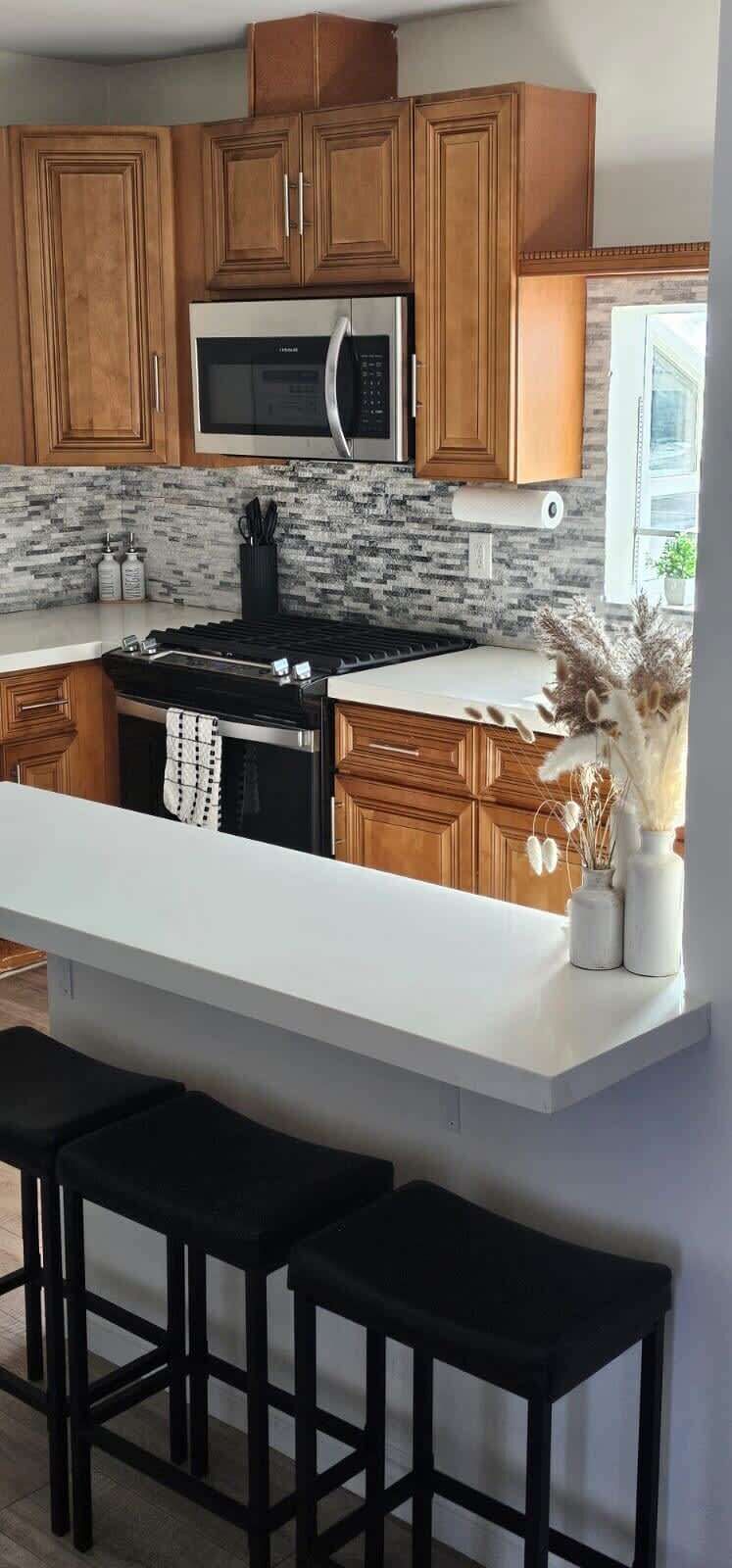 Une cuisine avec des meubles de rangement en bois, un four à micro-ondes, une cuisinière et un plan de travail blanc.