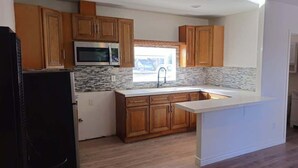 A kitchen with wooden cabinets, a microwave, a refrigerator, and a window. - Cozy Home Minutes to Beach Cities! (Paramount)