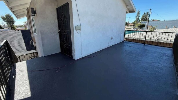 A rooftop with a flat surface, a black gate, and a white building with a door. - Cozy Home Minutes to Beach Cities! (Paramount)