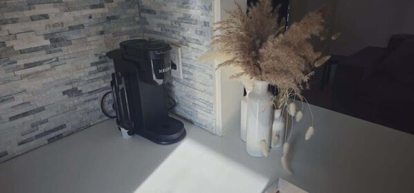 A coffee maker, a vase with dried plants, and a textured wall.