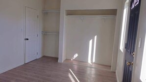 A room with a wooden floor, white walls, a closet with hanging space, and a door with a brass handle. - Cozy Home Minutes to Beach Cities! (Paramount)