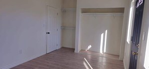 A room with a wooden floor, white walls, a closet with hanging space, and a door with a brass handle. - Cozy Home Minutes to Beach Cities! (Paramount)