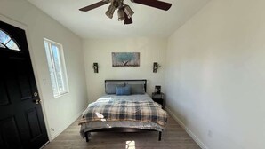 A bedroom with a bed, a ceiling fan, a painting on the wall, and a door. - Cozy Home Minutes to Beach Cities! (Paramount)