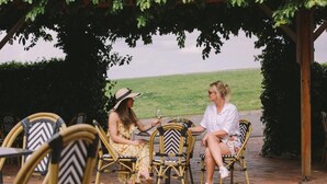 Two people sitting at a table under a pergola with chairs that have a chevron pattern. - Bimbadgen Estate (Pokolbin)