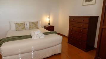 A neatly made bed with a green throw, a bedside table with a lamp, and a wooden dresser.
