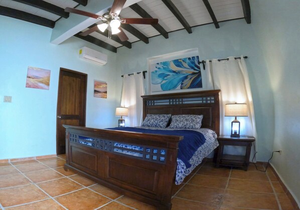 A bedroom with a wooden bed, two bedside lamps, a ceiling fan, and a large abstract painting on the wall. - Mermaid’s Hideaway—2 bedroom, 2 bath
3 minute walk to stunning West Bay Beach (West Bay)