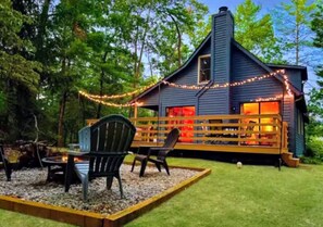 A cozy cabin with a deck, surrounded by trees.