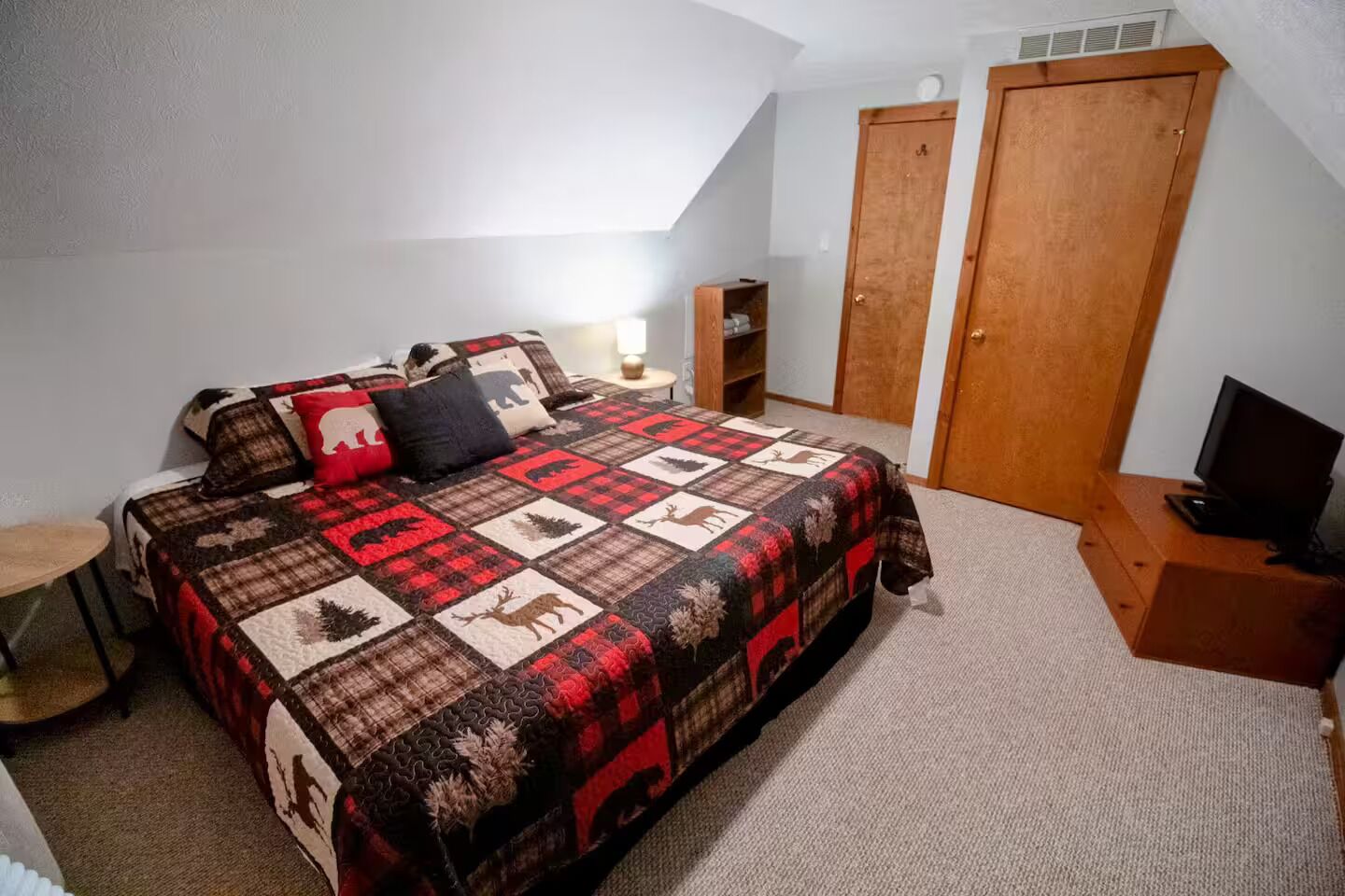 Une chambre avec un grand lit, un téléviseur posé sur un meuble en bois, une armoire et une petite table.