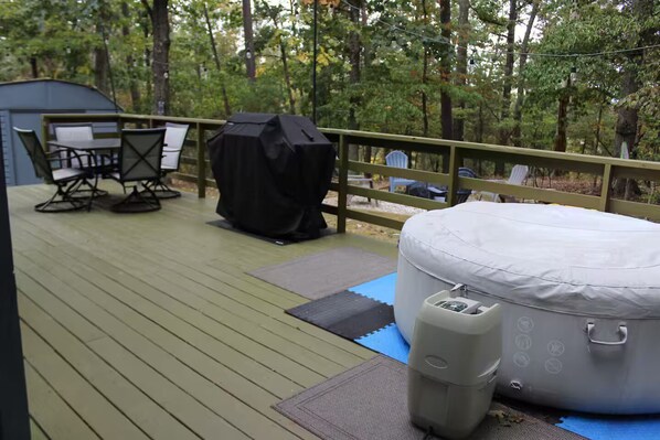 A deck with a covered grill, a table with chairs, a covered sofa, and a trash can.