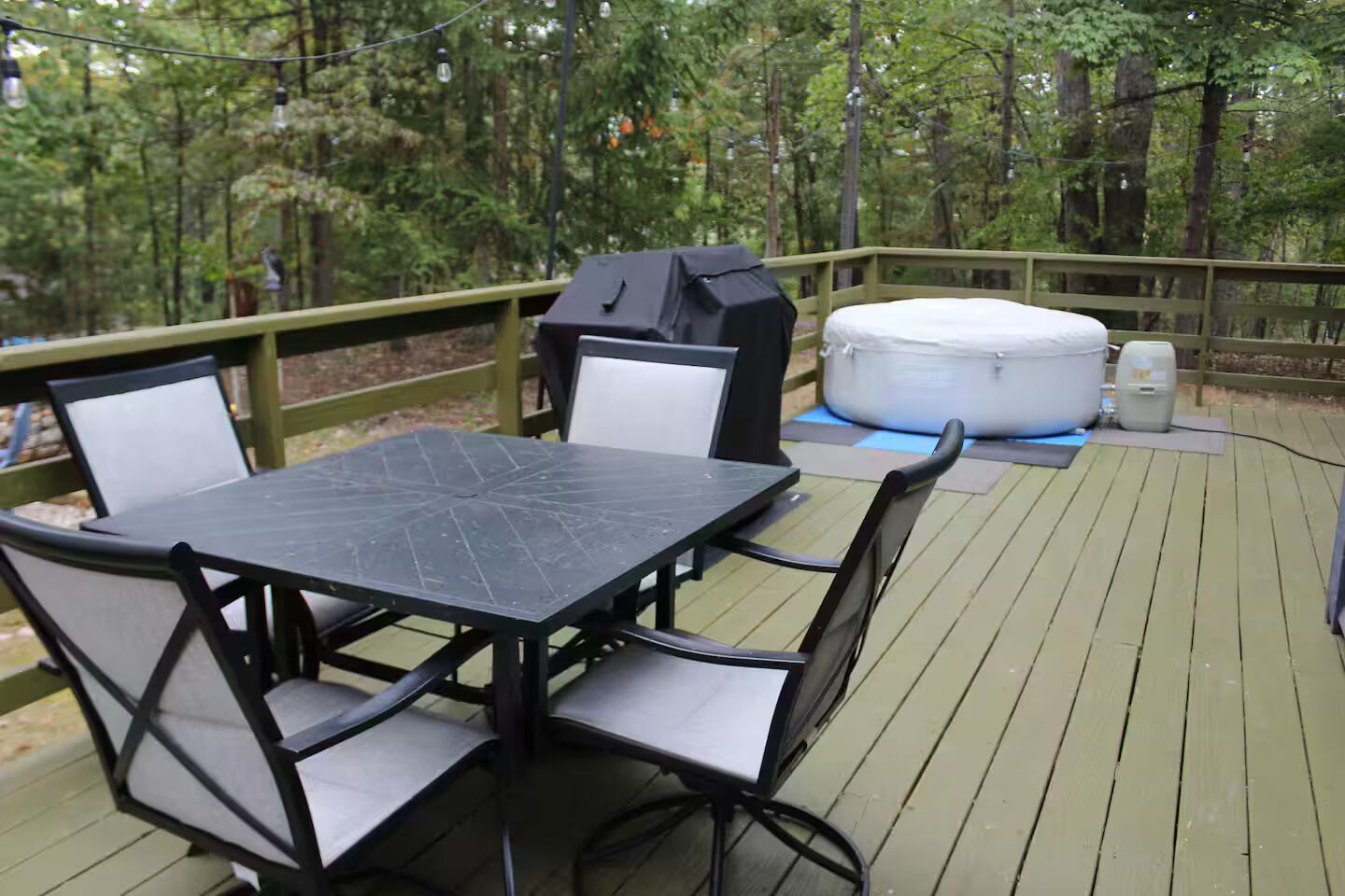 Een terras met tafel, stoelen, een barbecue en een hottub.