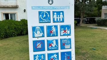 Señal con las normas de la piscina: horario de funcionamiento, prohibido topless, prohibido topless, prohibido bucear y prohibido nadar.