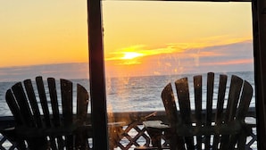 Two Adirondack chairs facing a sunset over the ocean.