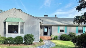 A single-story house with a green metal roof, a front porch, and a gravel driveway.