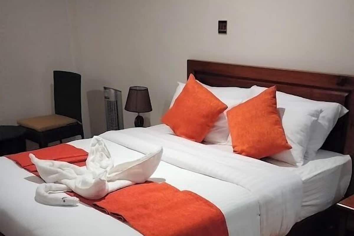 Una cama bien tendida con ropa de cama blanca y naranja, un cabecero de madera y un cuadro enmarcado en la pared.