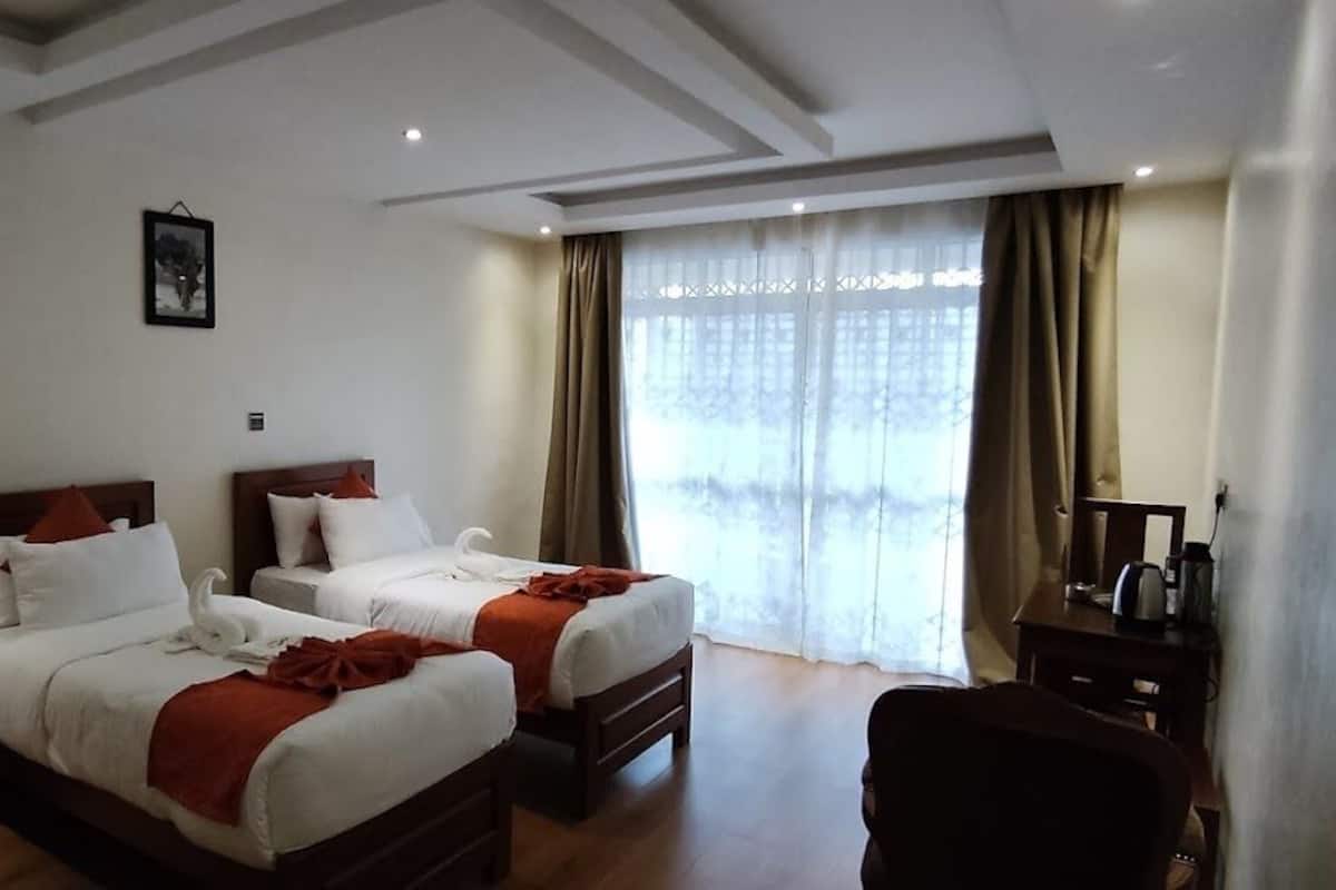 Habitación de hotel con dos camas, un escritorio y un ventanal grande con cortinas.