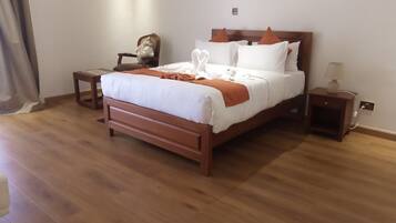 Una cama bien hecha con ropa de cama blanca y naranja, una mesita de noche de madera con una lámpara y una pequeña silla de madera.