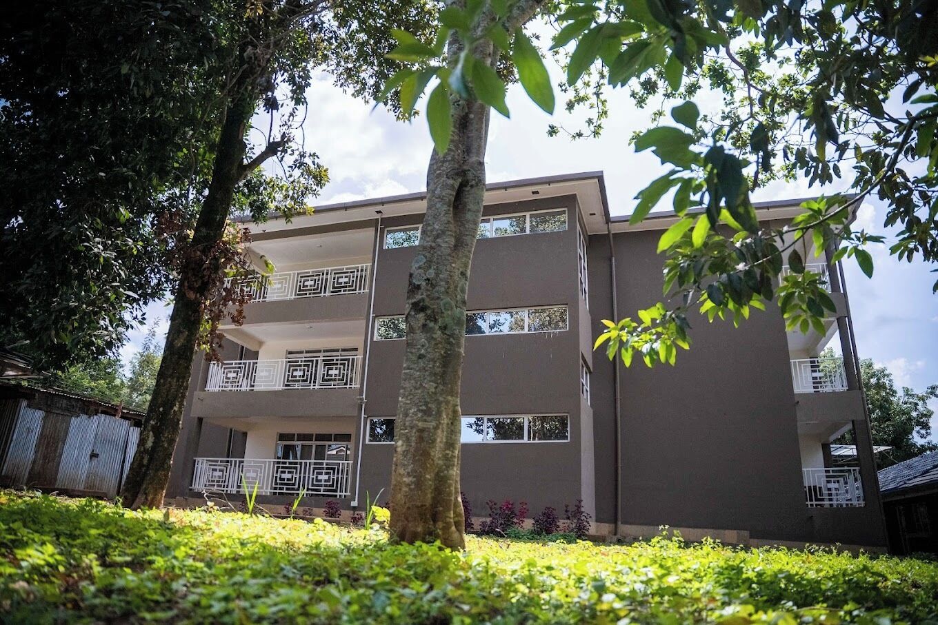 A multi-story building with balconies and a garden area in front.