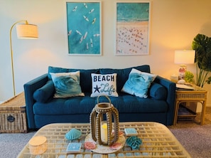 A living room with a blue sofa, a coffee table with decorative items, and wall art depicting beach scenes.