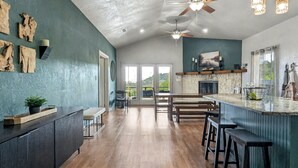 Une cuisine spacieuse avec un plancher en bois, un coin bar avec des tabourets et un ventilateur de plafond.