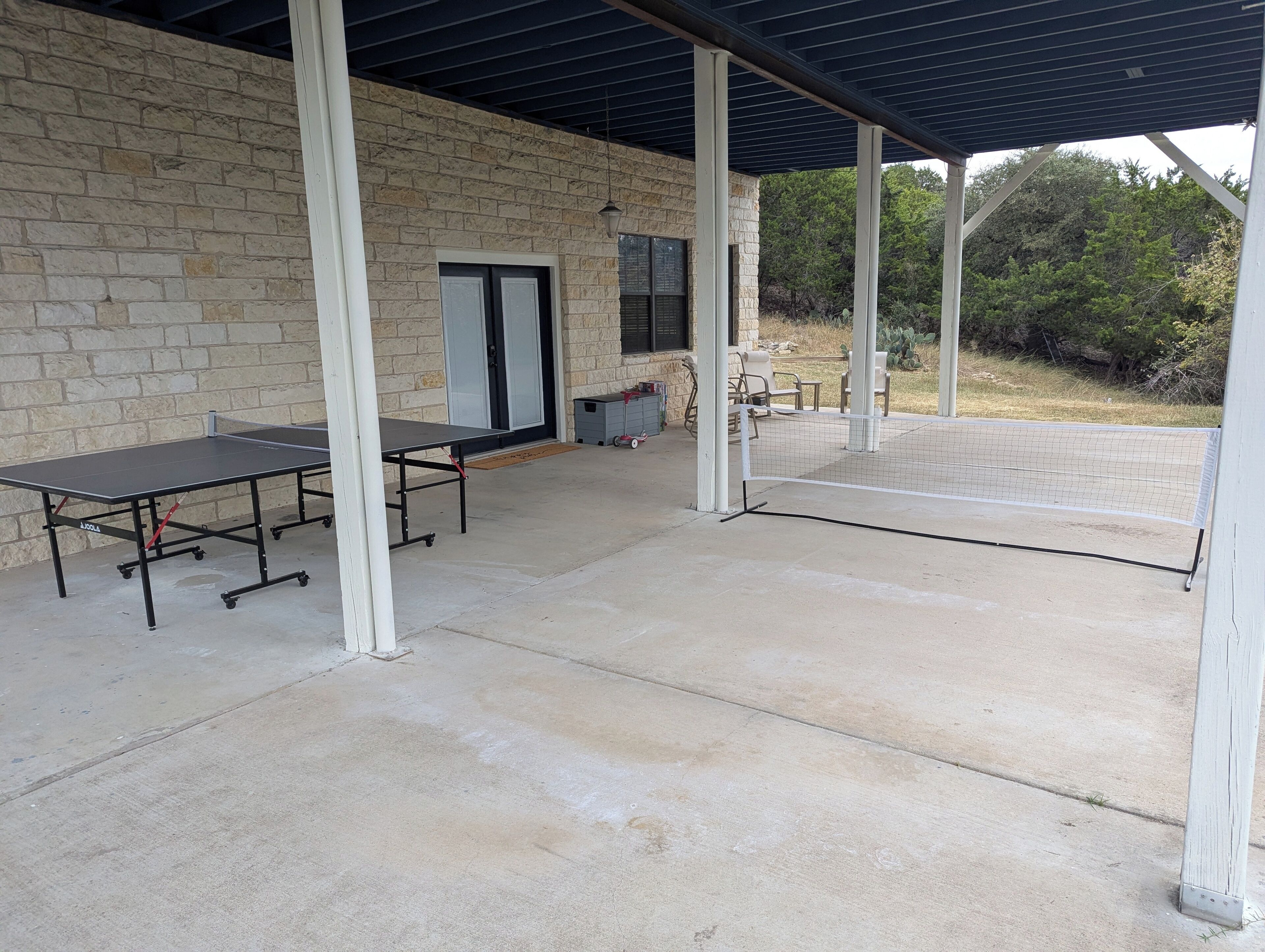 Un espacio al aire libre techado con mesa de ping pong, pared de piedra y una puerta.