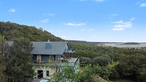 Une maison dotée d’un balcon, entourée d’arbres et de collines, et offrant une vue sur une étendue d’eau.