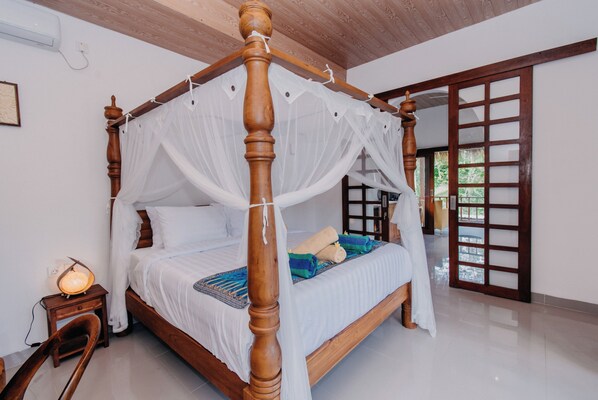 Una cama con dosel, una mesita de noche con lámpara, y vista al exterior por una puerta de madera.