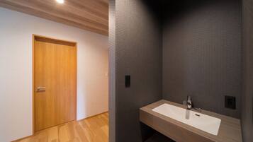 Un baño moderno con una puerta de madera, un lavabo blanco y una pared oscura con textura.