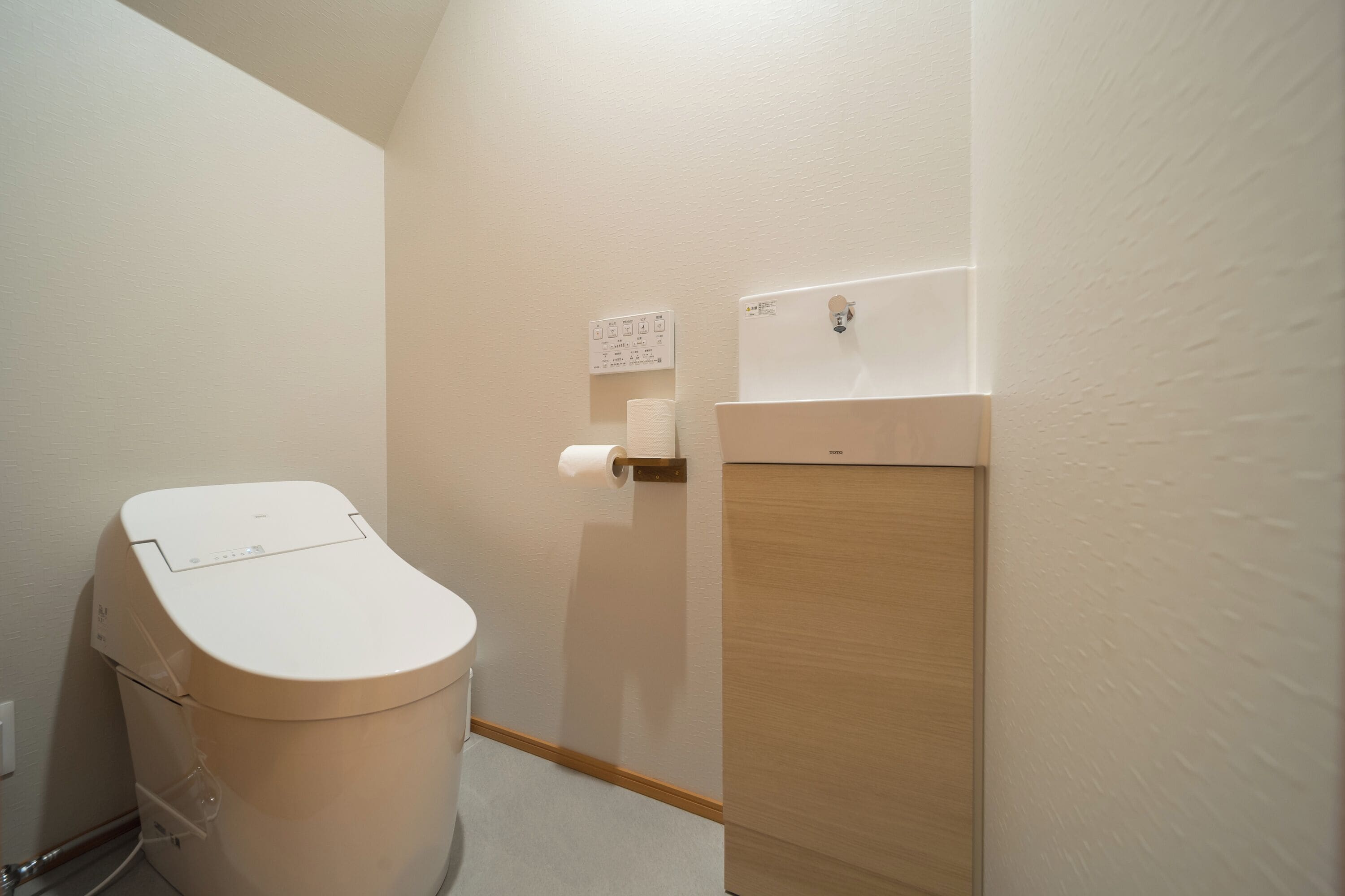 A compact bathroom with a toilet, a paper towel dispenser, and a wall-mounted electrical outlet.
