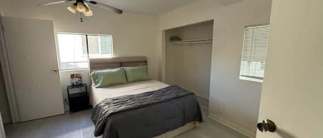 Ein Schlafzimmer mit Bett, Deckenventilator, Nachttisch, Fenster und Tür.
