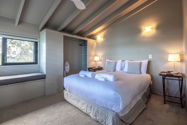 A bedroom with a large bed, bedside lamps, a window, and a walk-in closet. - Spinnaker Watch - Waiheke Island (Waiheke Island)