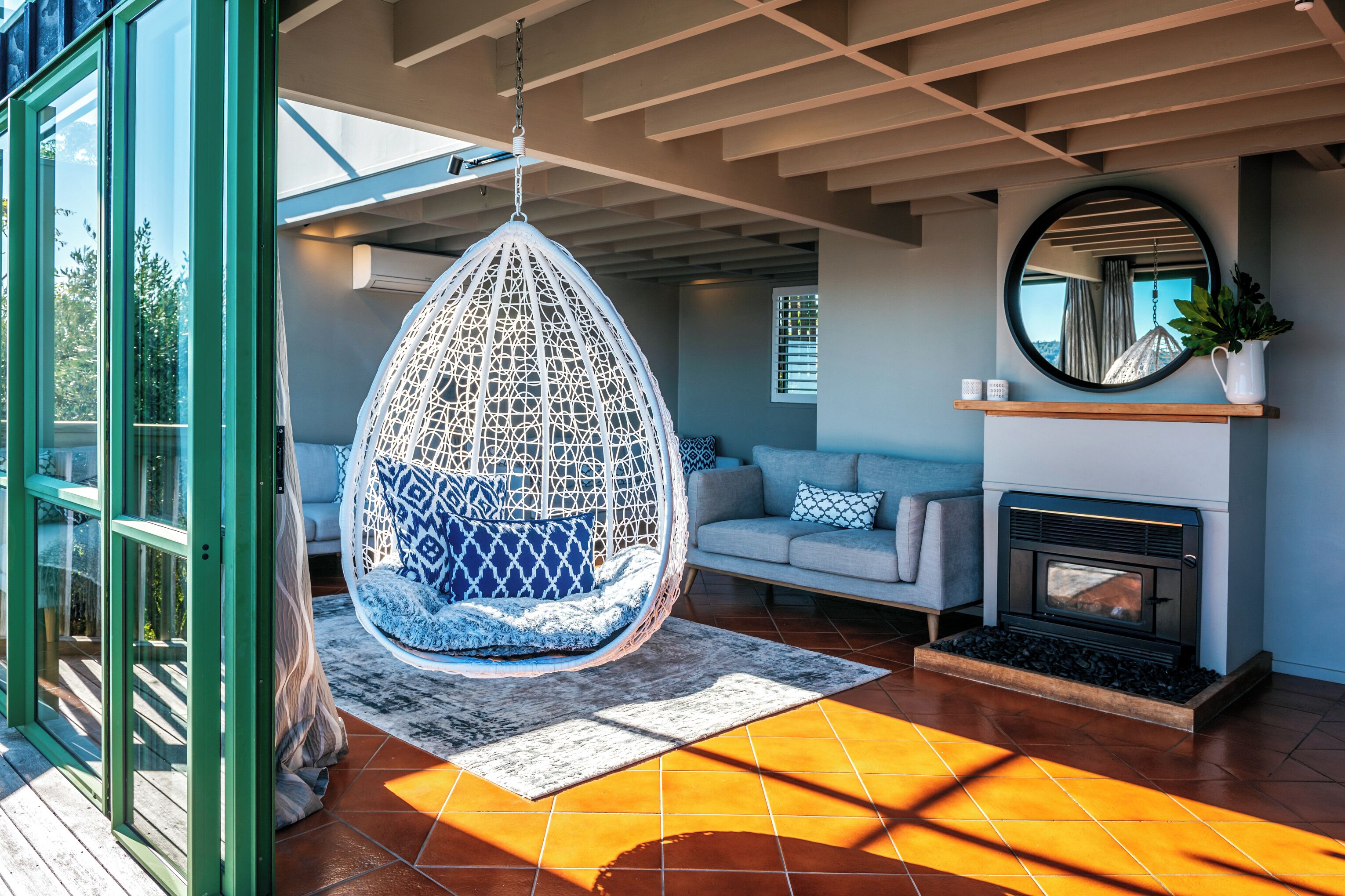 Una sala de estar moderna con un sillón colgante, chimenea, sofá y un espejo grande.