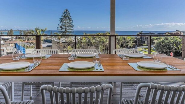A dining area with a wooden table set for four, overlooking a scenic view of the ocean and palm trees.