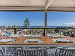 A dining area with a wooden table set for four, overlooking a scenic view of the ocean and palm trees. - Humpback Villa by Holiday Management Co. (Tweed)