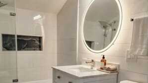 Une salle de bain moderne avec un meuble-lavabo blanc, un miroir rond, une baignoire et des toilettes.