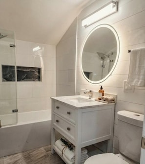 Une salle de bain moderne avec un meuble-lavabo blanc, un miroir rond, une baignoire et des toilettes.
