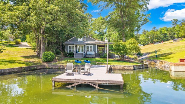 A house with a dock extending into a pond, surrounded by greenery and trees.