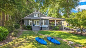 A house with a porch, a grill, and two kayaks on the lawn.