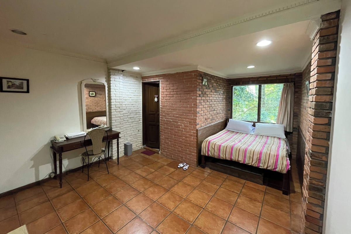 A bedroom with a bed, a desk, a chair, and a window.