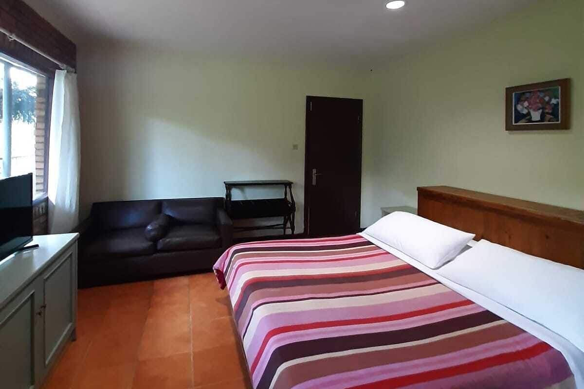 A bedroom with a bed, a sofa, a television, and a door.