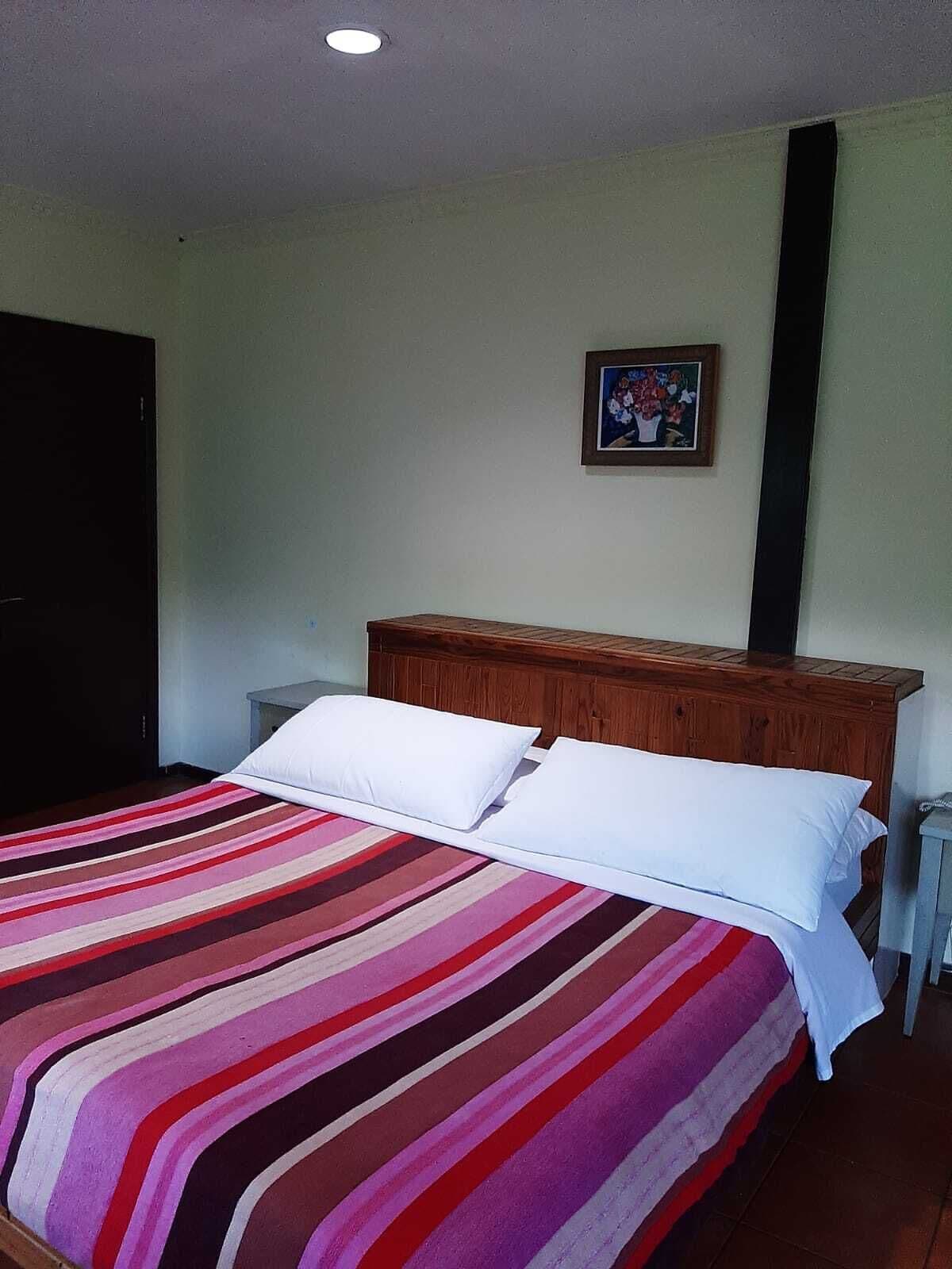 A room with a bed, a wooden headboard, a small bedside table, and a framed picture on the wall.